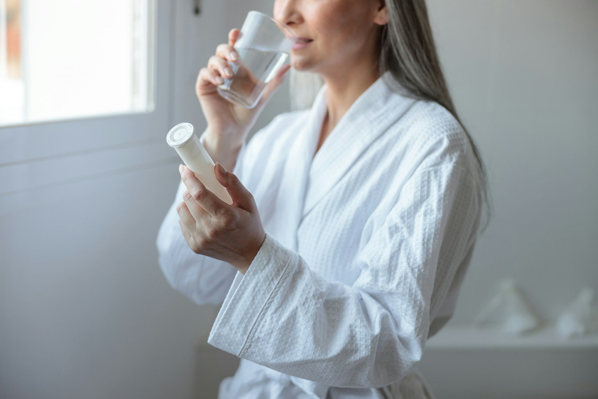 Beautiful woman in white bathrobe taking vitamins