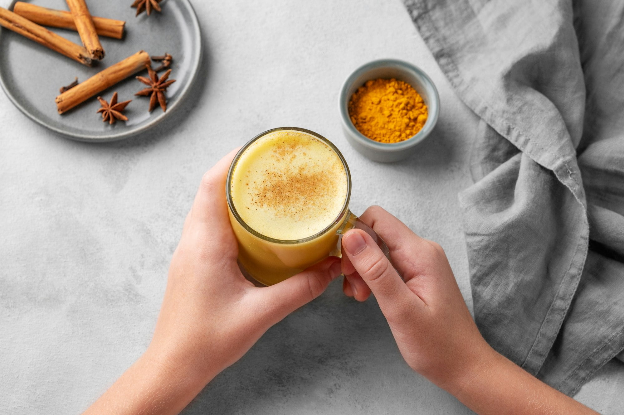 Hands holding turmeric golden milk latte with spices and honey. Detox, immunity boosting